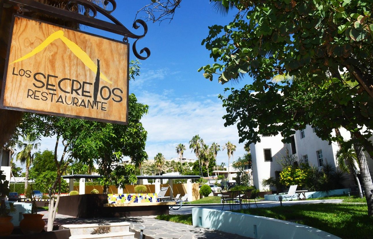 A sign for los secretos restaurant hangs from a tree