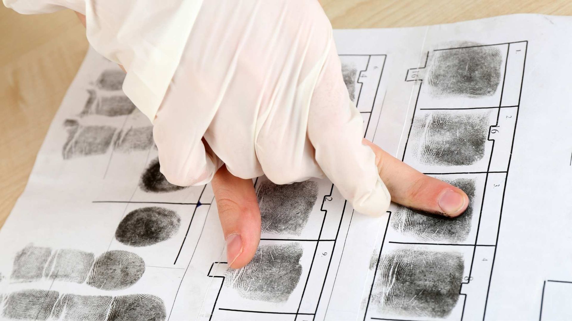 Gloved hand pointing to a fingerprint on a fingerprint card.