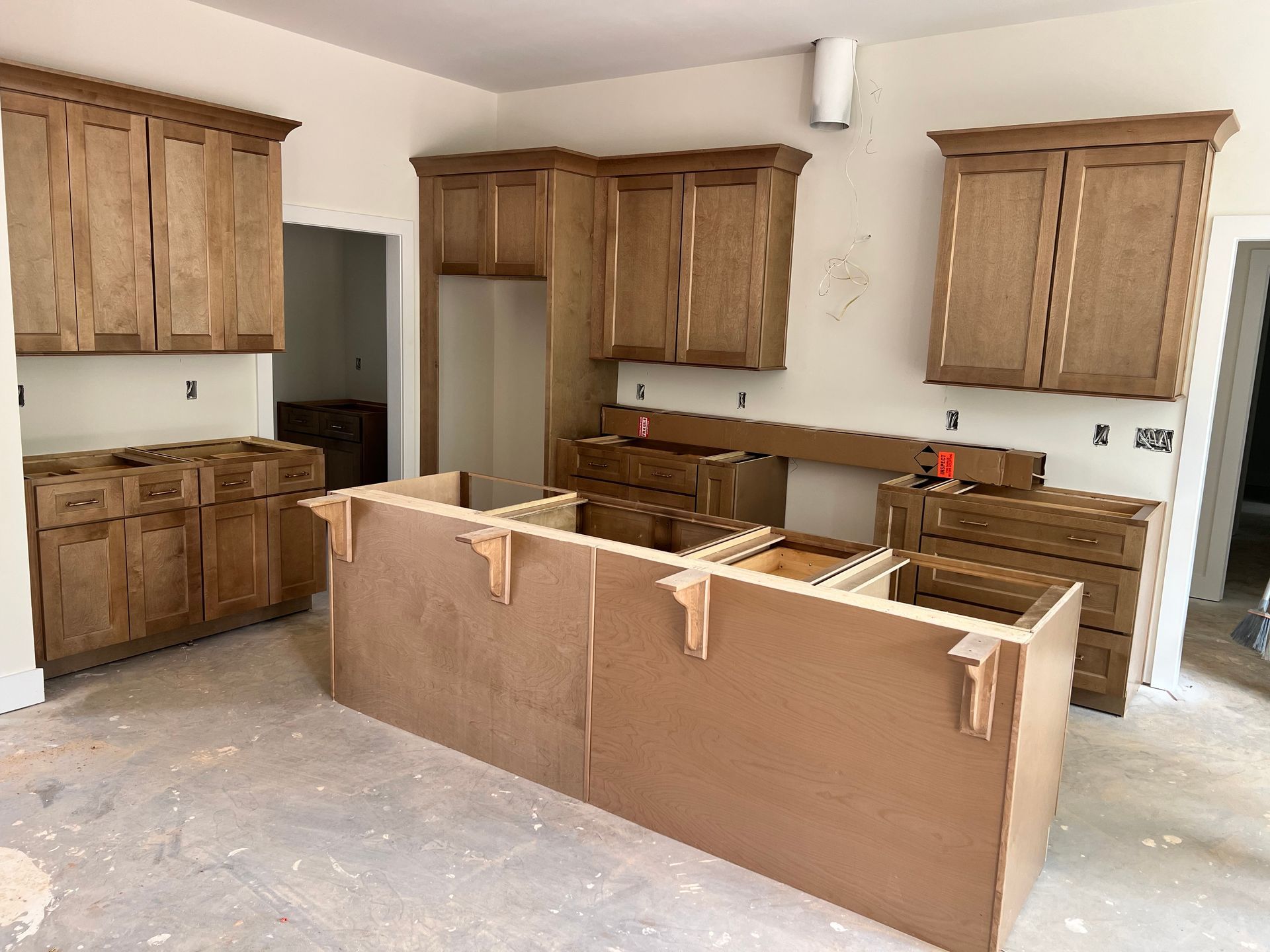 Kitchen cabinets in various stages of installation, with an island counter in the foreground. Unfinished interior.
