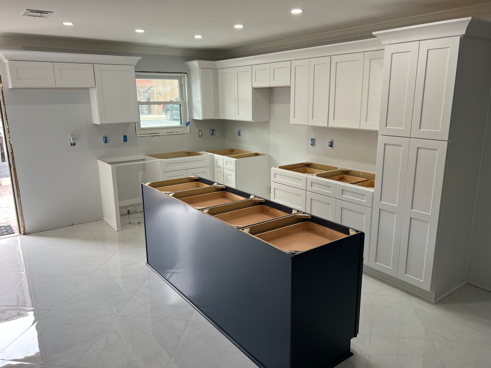 Kitchen under construction with white cabinets, dark blue island, and white floors.