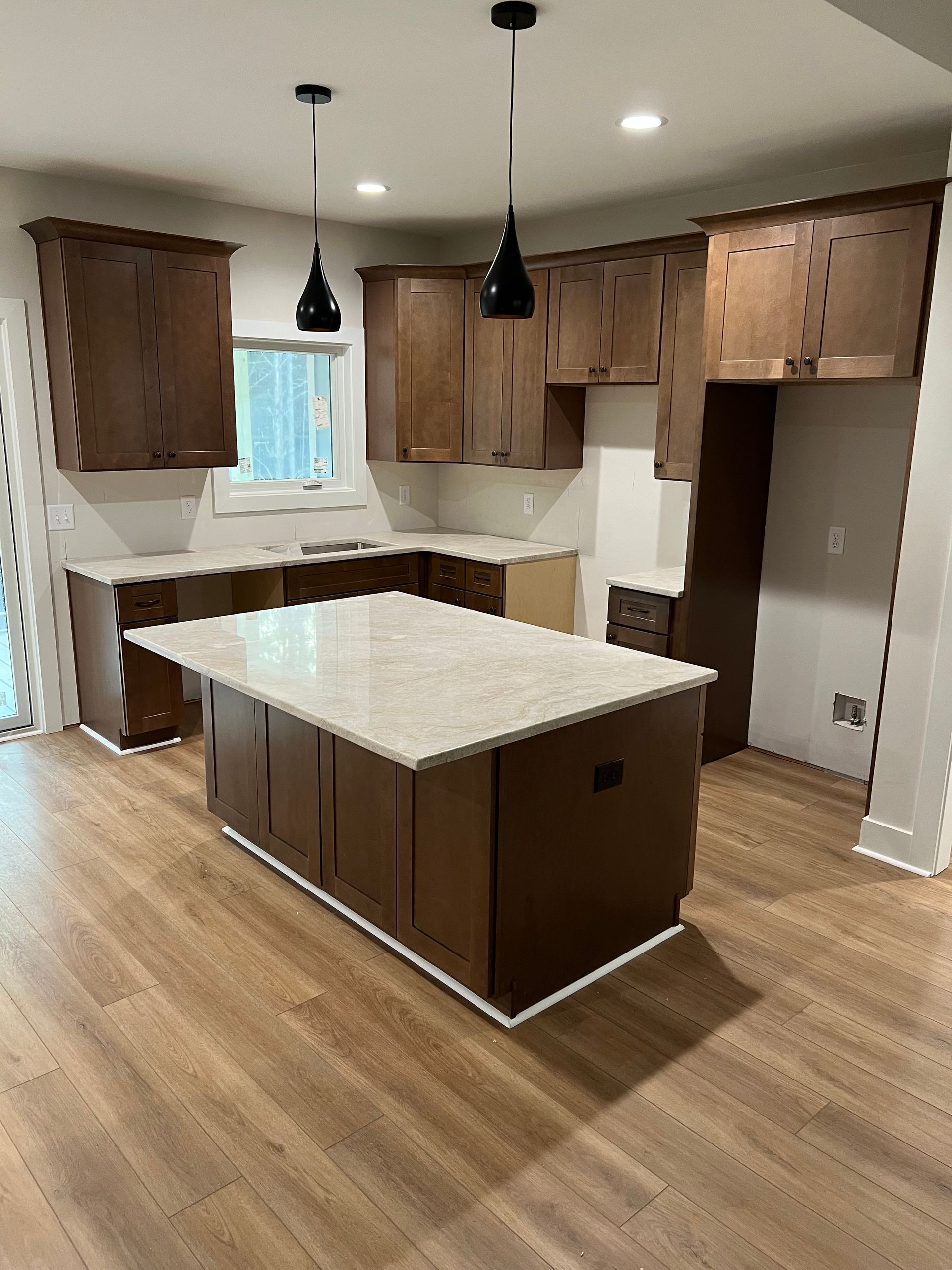 Kitchen with brown cabinets, a white countertop island, and black pendant lights.