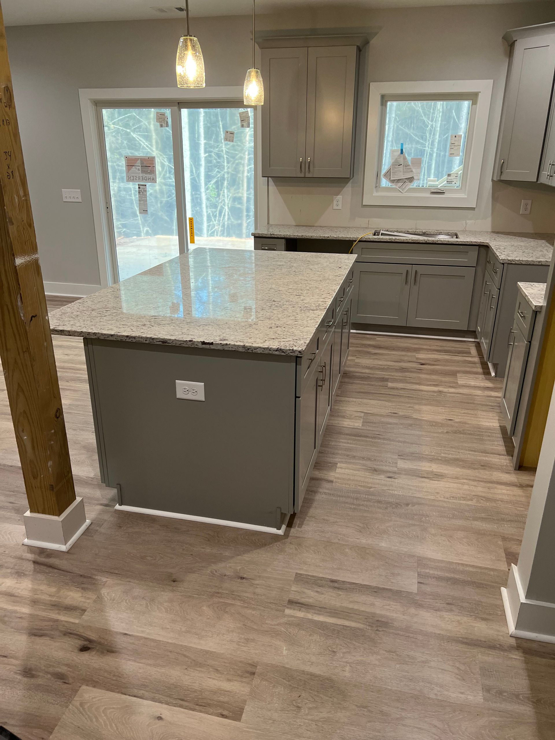 Grey kitchen with island, cabinets, and granite countertops, light wood floor, and sliding glass door.