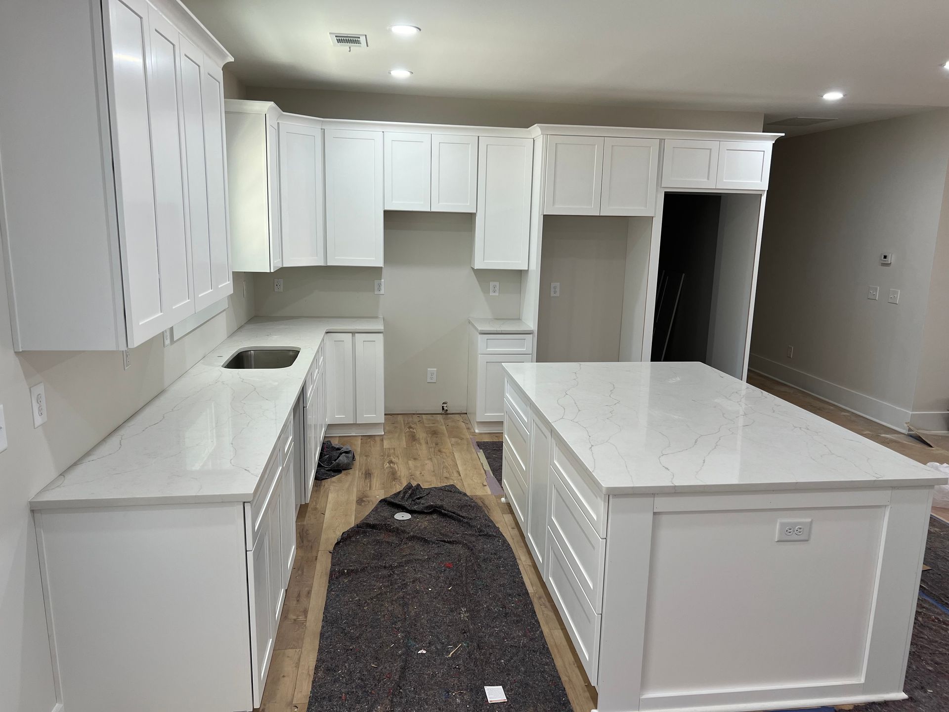 White kitchen with island and cabinets, quartz countertops. Under construction, wood floors.