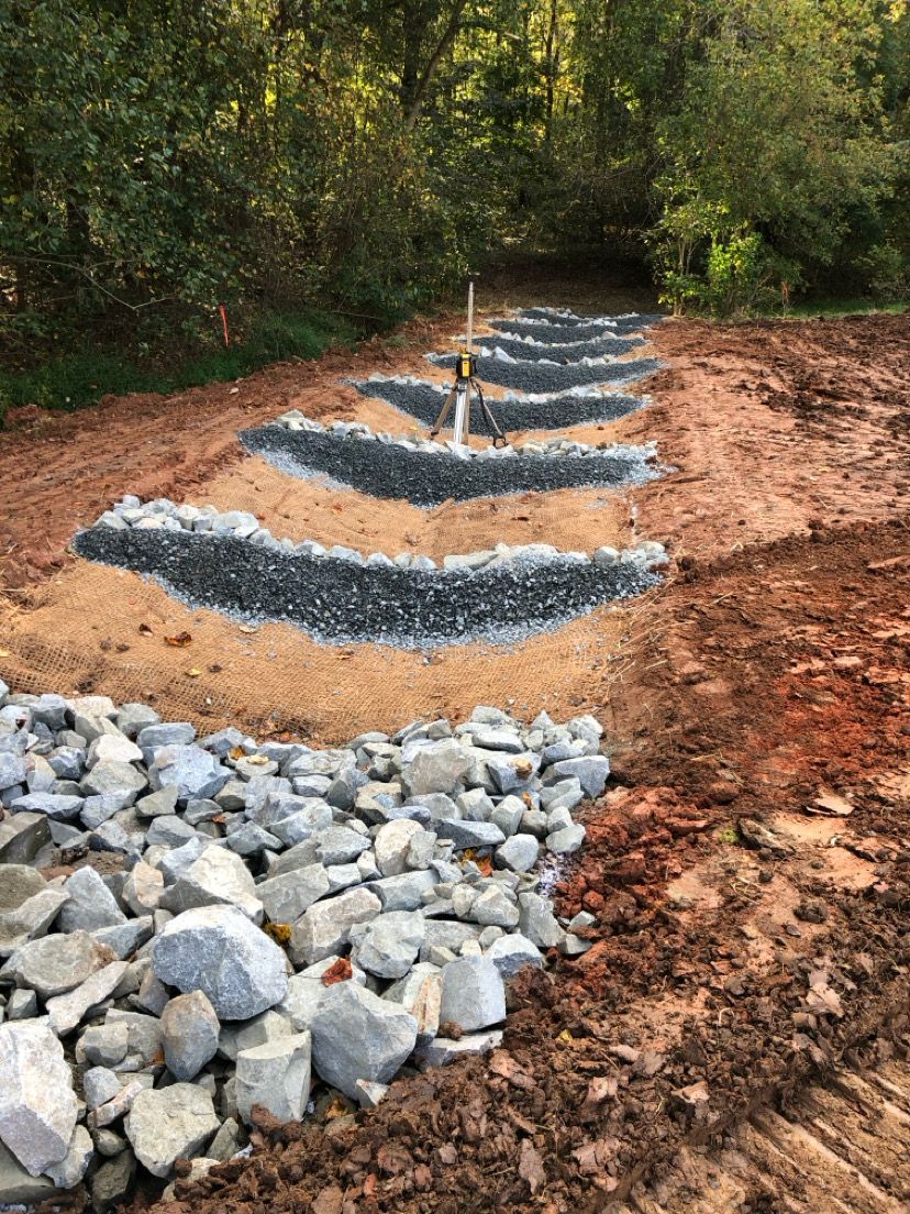 Terraced stone drainage path under construction along a wooded dirt slope