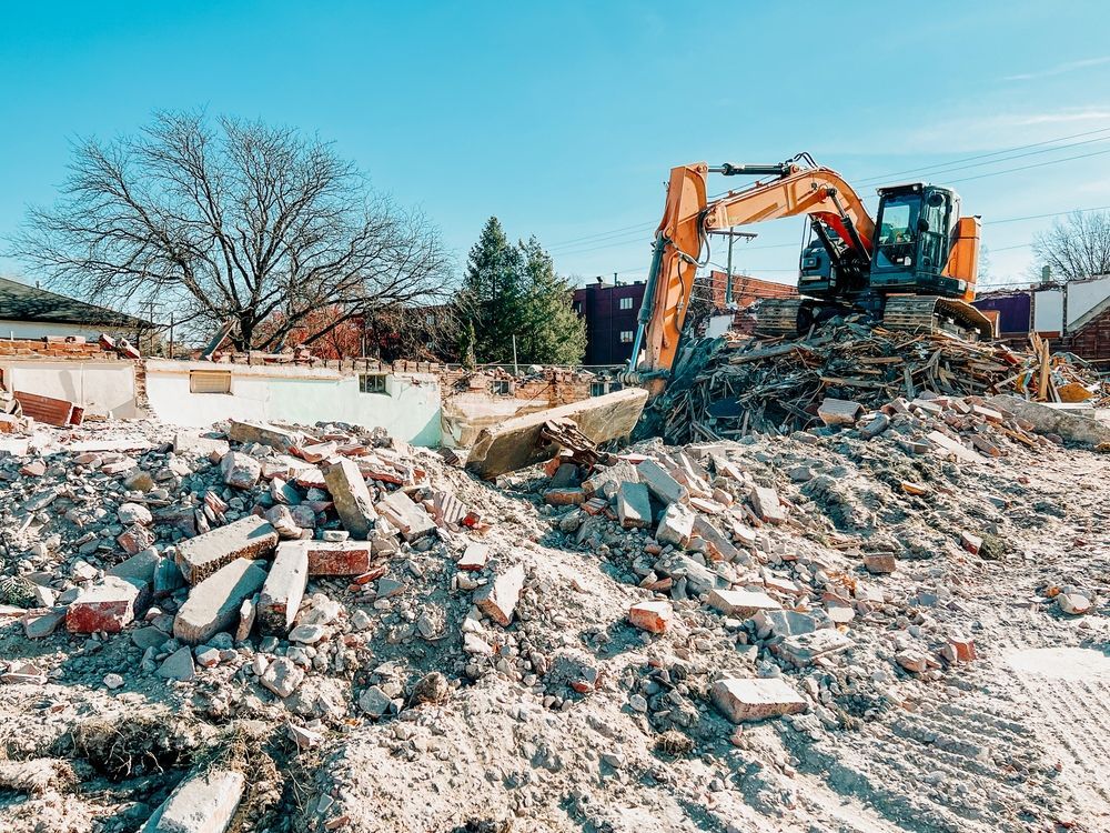 Excavator clearing rubble at a demolition site under a clear sky