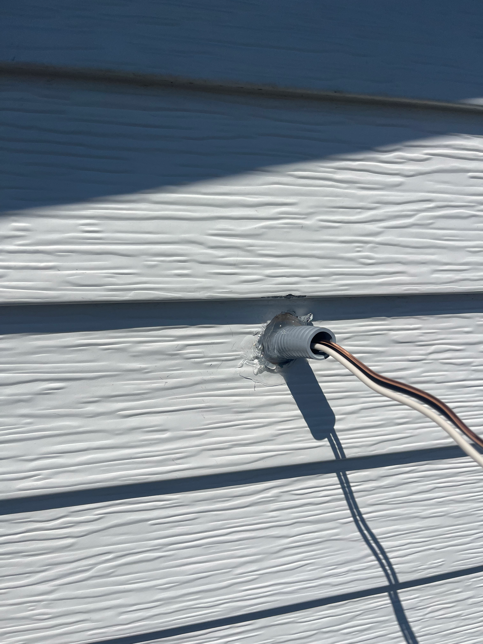 Gray electrical conduit and wires protruding from siding on a building exterior.