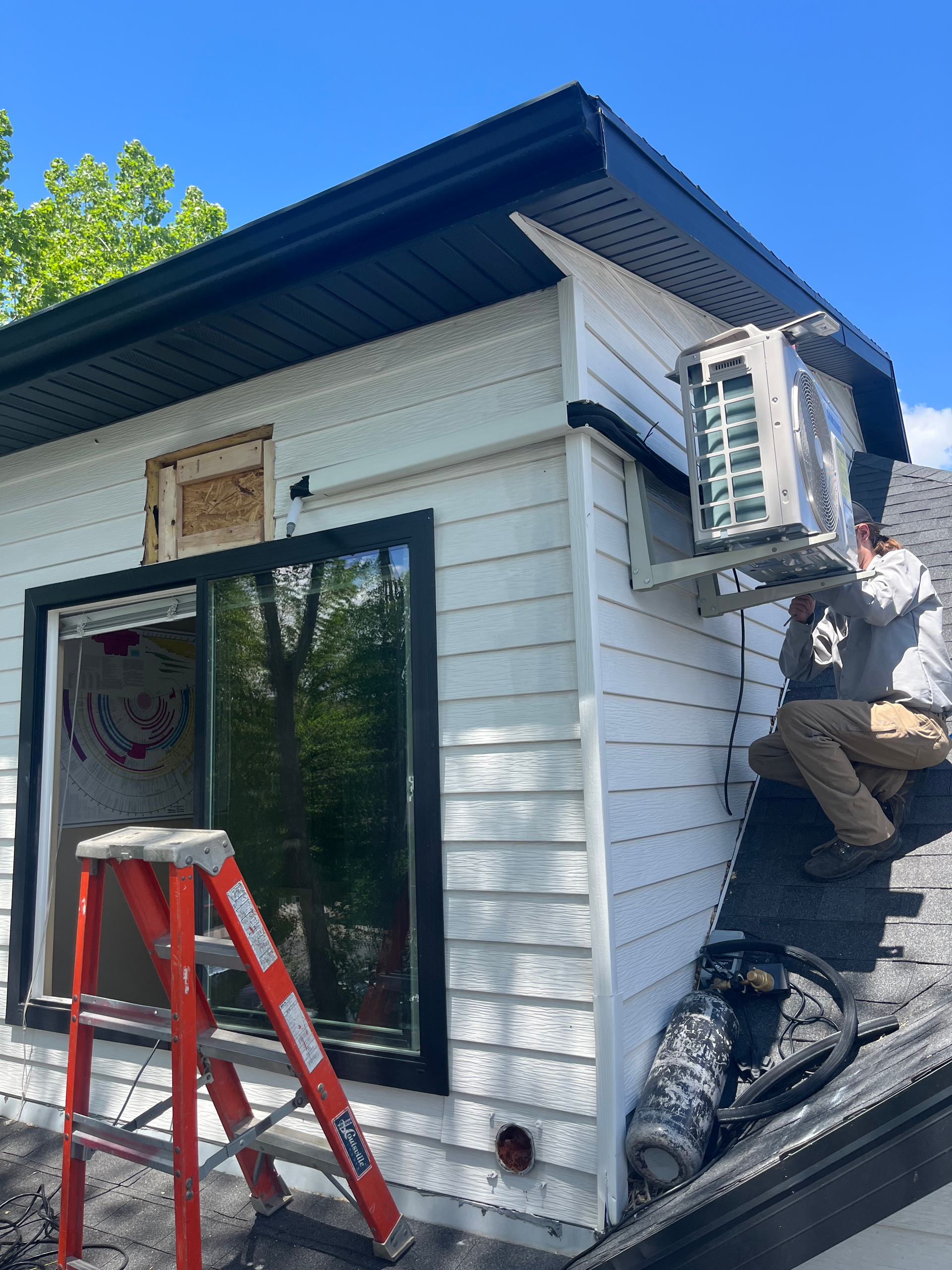 Workers installing an air conditioning unit on a white building with a black roof and trim.