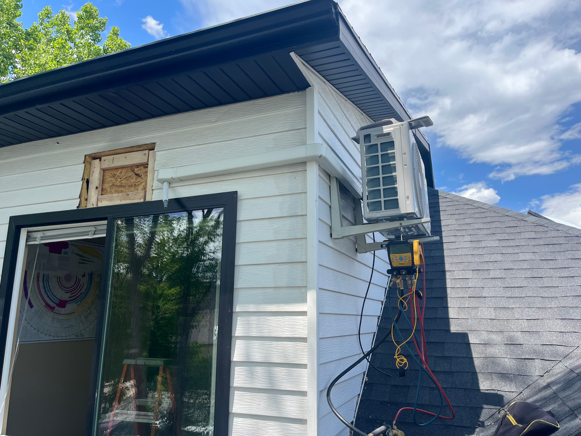 White building exterior with a mounted air conditioner, wires, and a glass sliding door.
