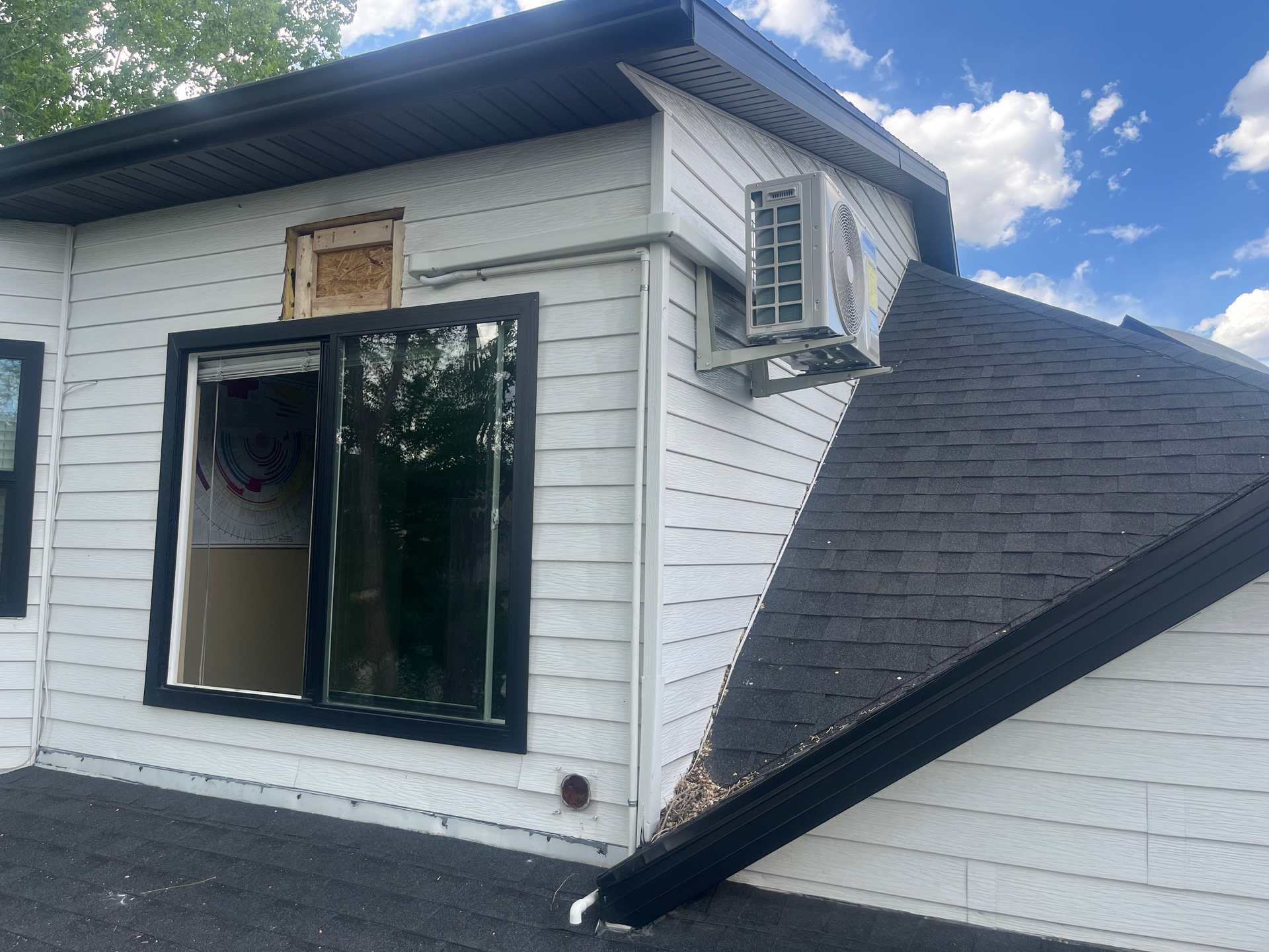 Exterior of a white house with black trim, a window, and an air conditioning unit. Dark roof in the foreground.