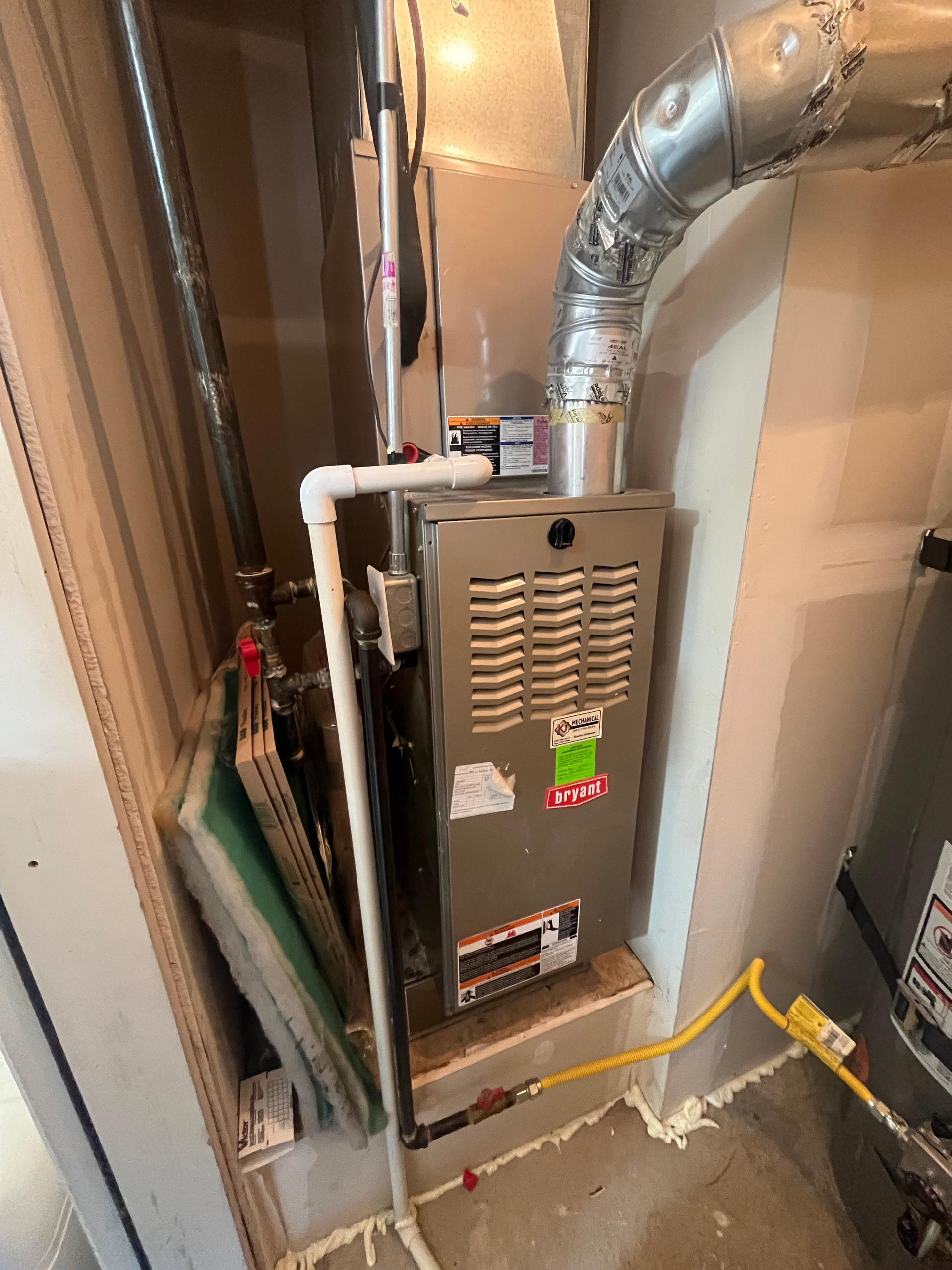 Furnace installed in a utility closet with vent and gas line, white and gray.
