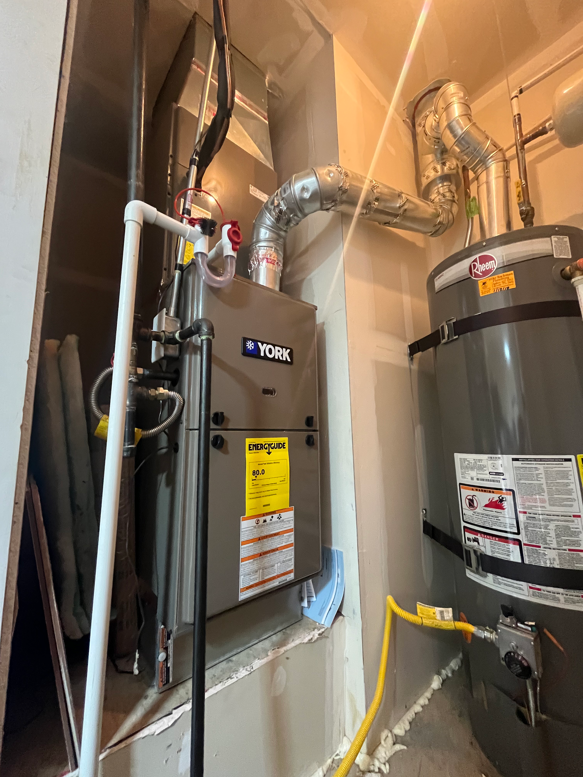 Furnace and water heater in a utility closet. Gray and silver appliances. White pipes and yellow electrical cable visible.
