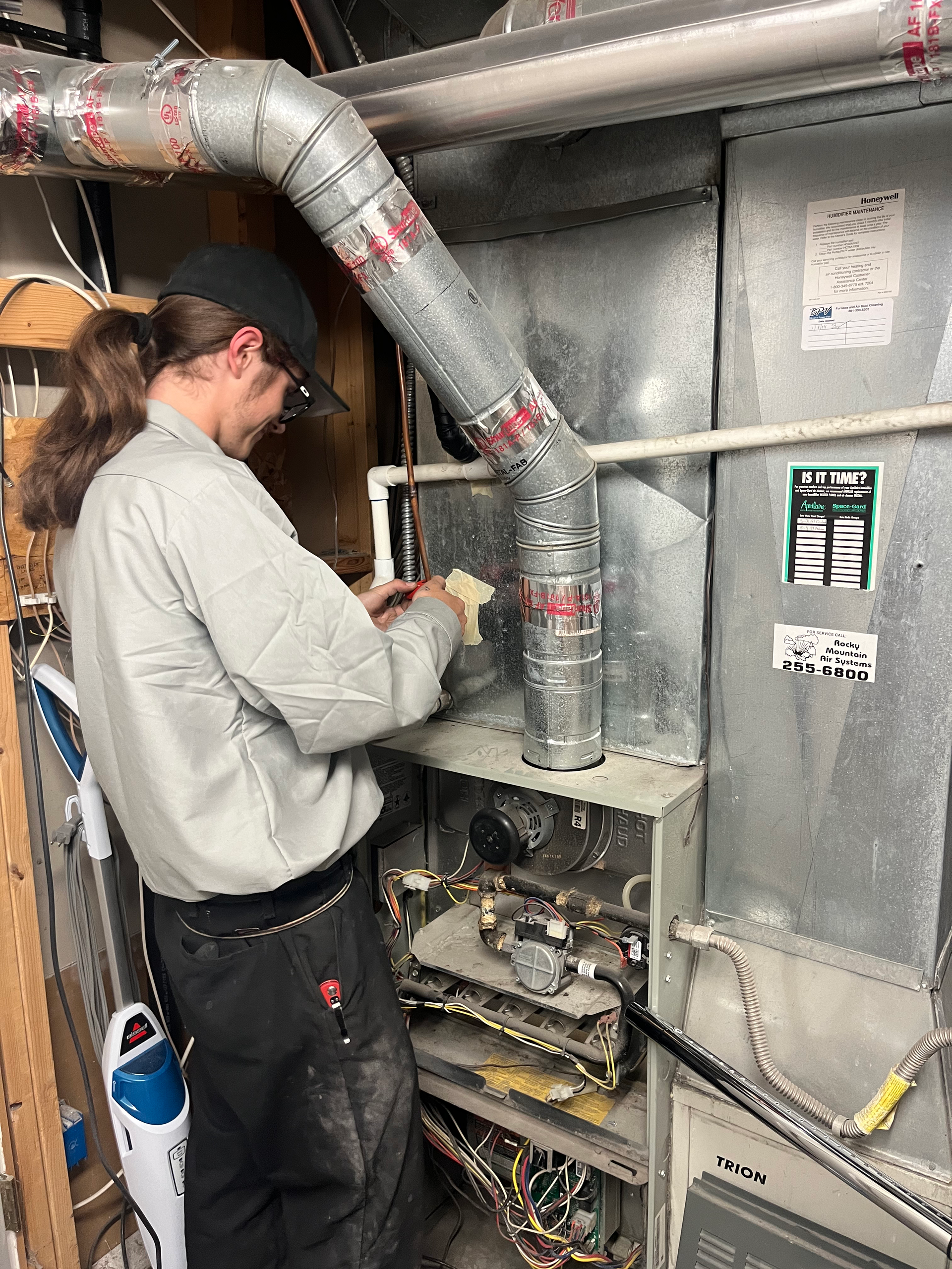 Man in work clothes working on a furnace, in a basement setting.