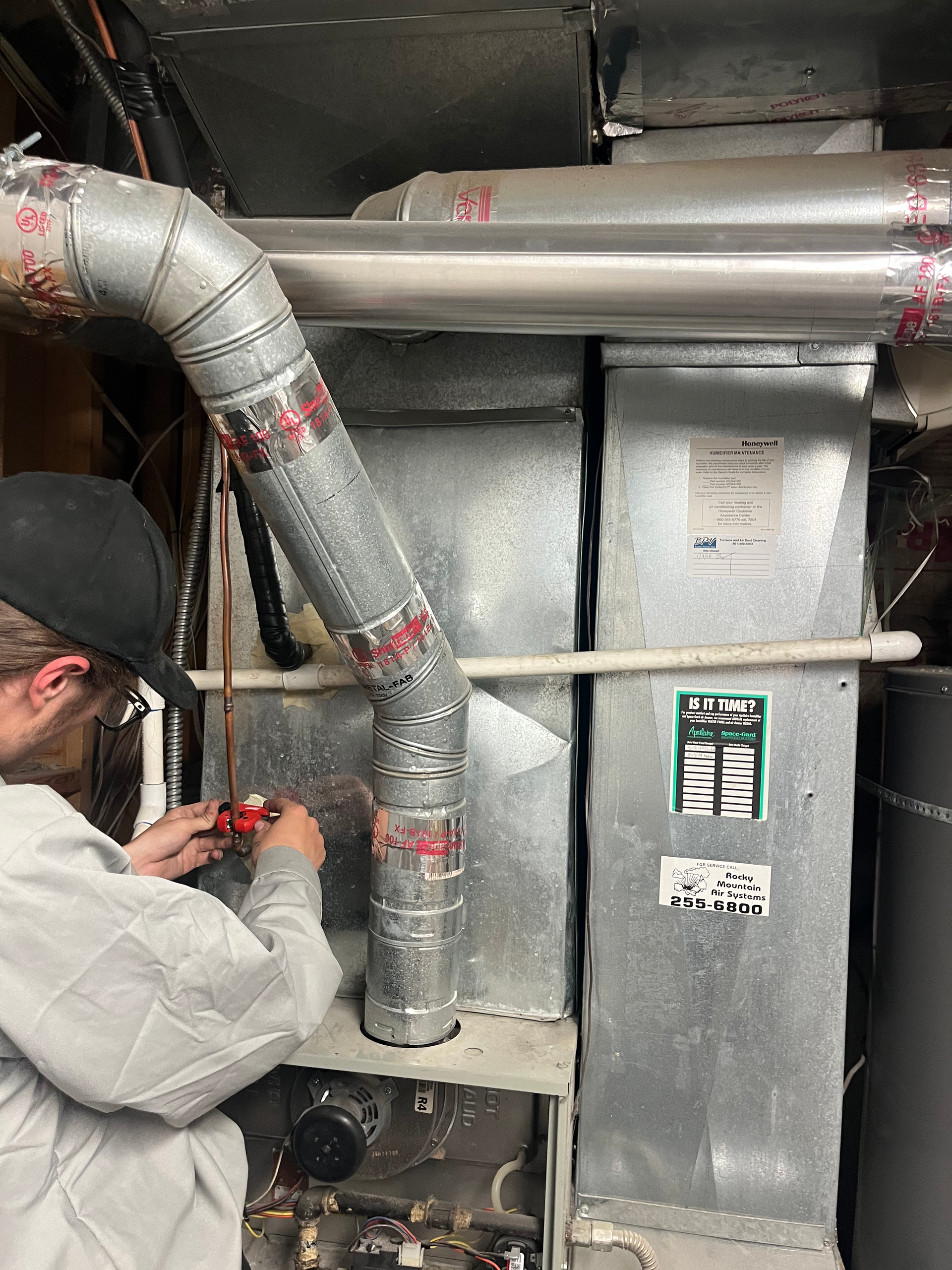 Person in work clothes using a tool on ductwork connected to a metal furnace.
