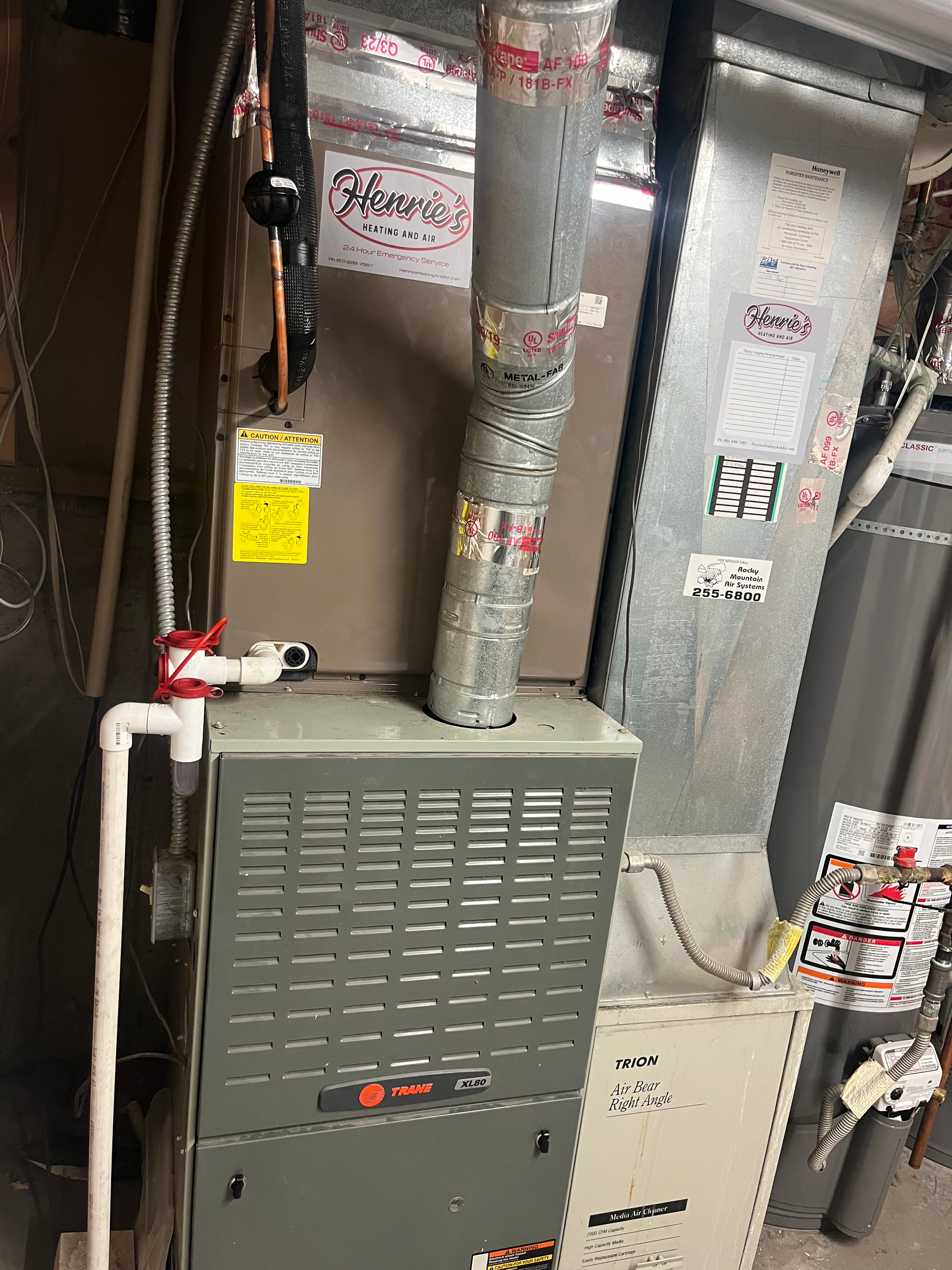 Furnace unit with ductwork, piping, and labels in a utility room.