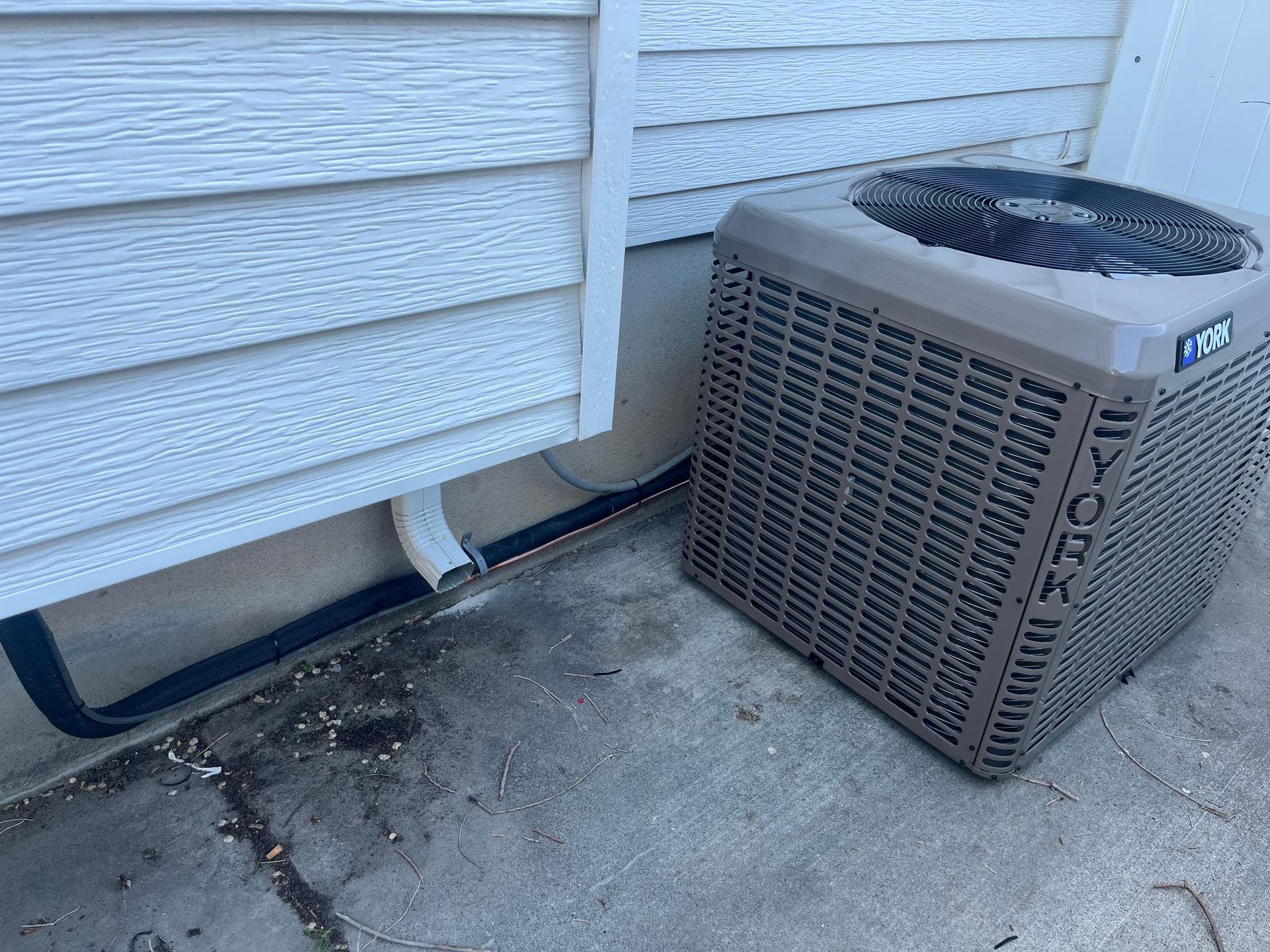 An air conditioning unit next to a house with white siding and a concrete slab.