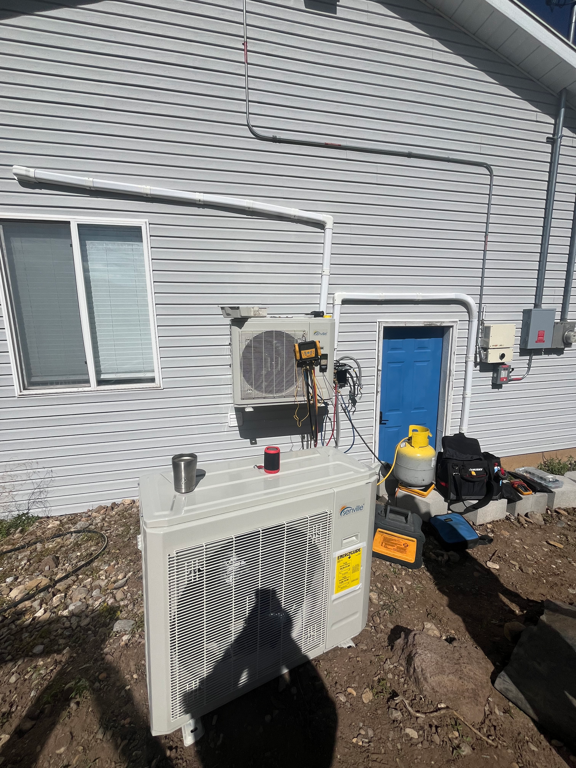 Outdoor heat pump unit and electrical components mounted on a house exterior.