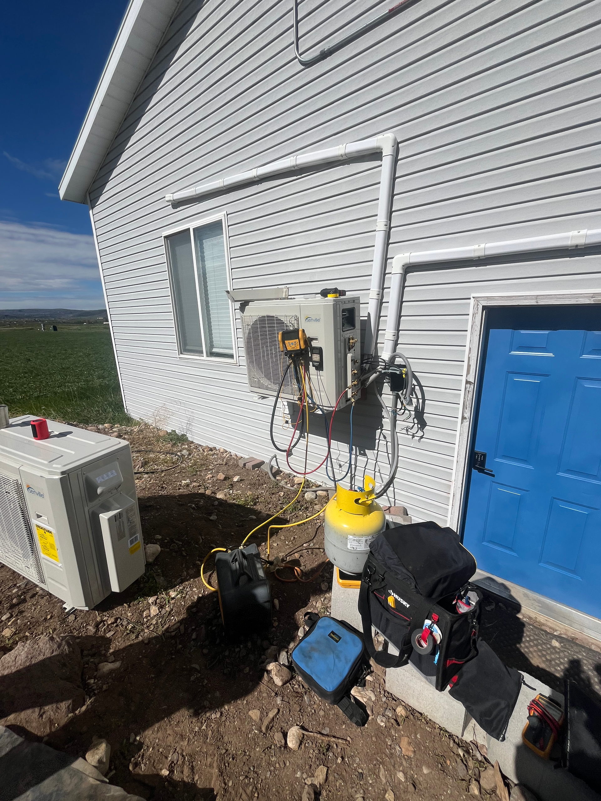 HVAC unit installation. An exterior white building with an installed unit, tools, and a yellow refrigerant tank.