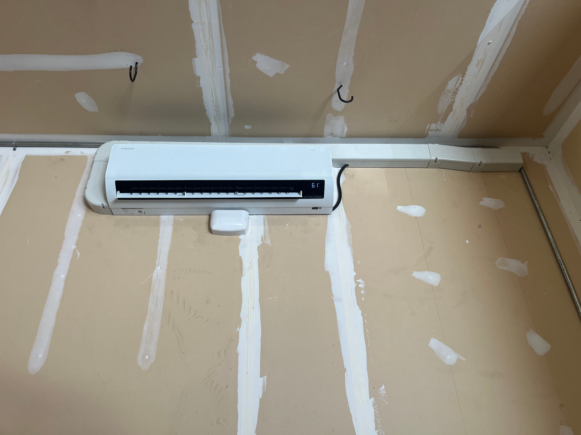 White mini-split air conditioner mounted on a beige wall, installed in a room under construction.