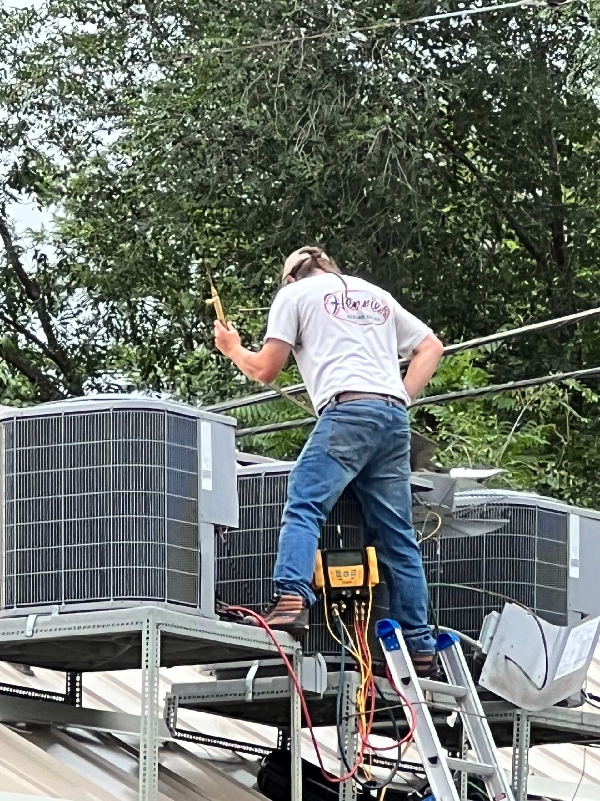 HVAC technician on a ladder, working on rooftop air conditioning units.