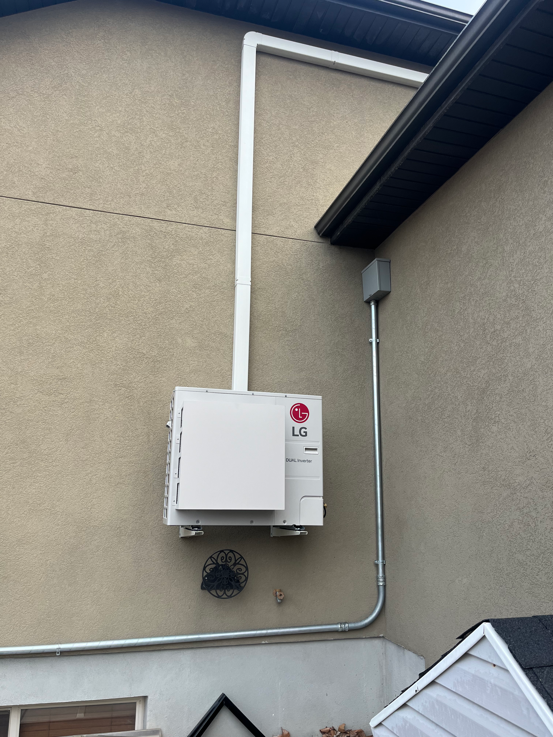 White electrical box mounted on a beige building exterior with conduit running to the roof and a gray box.