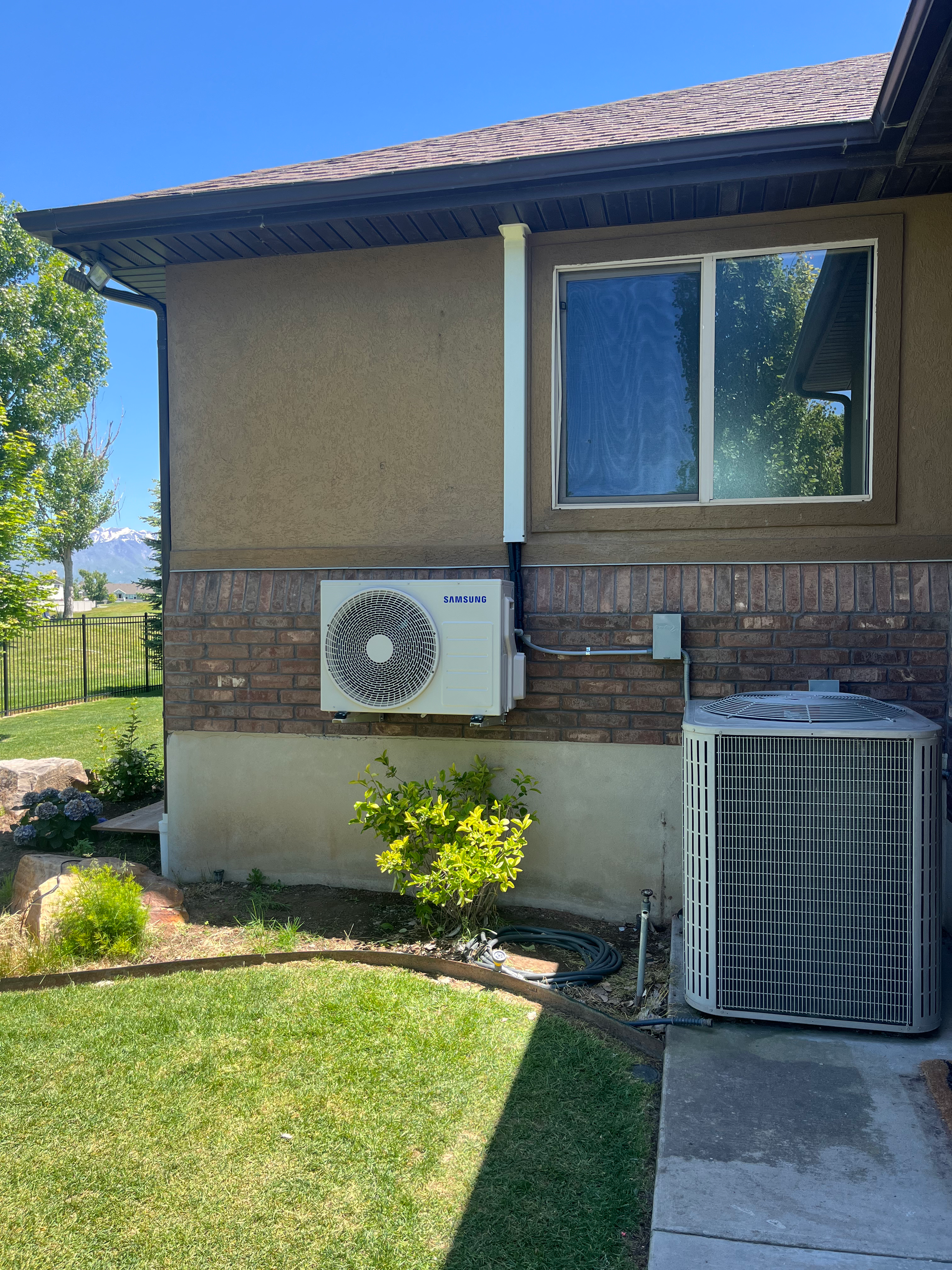 An HVAC system with outdoor units installed on a brick wall with a window above.