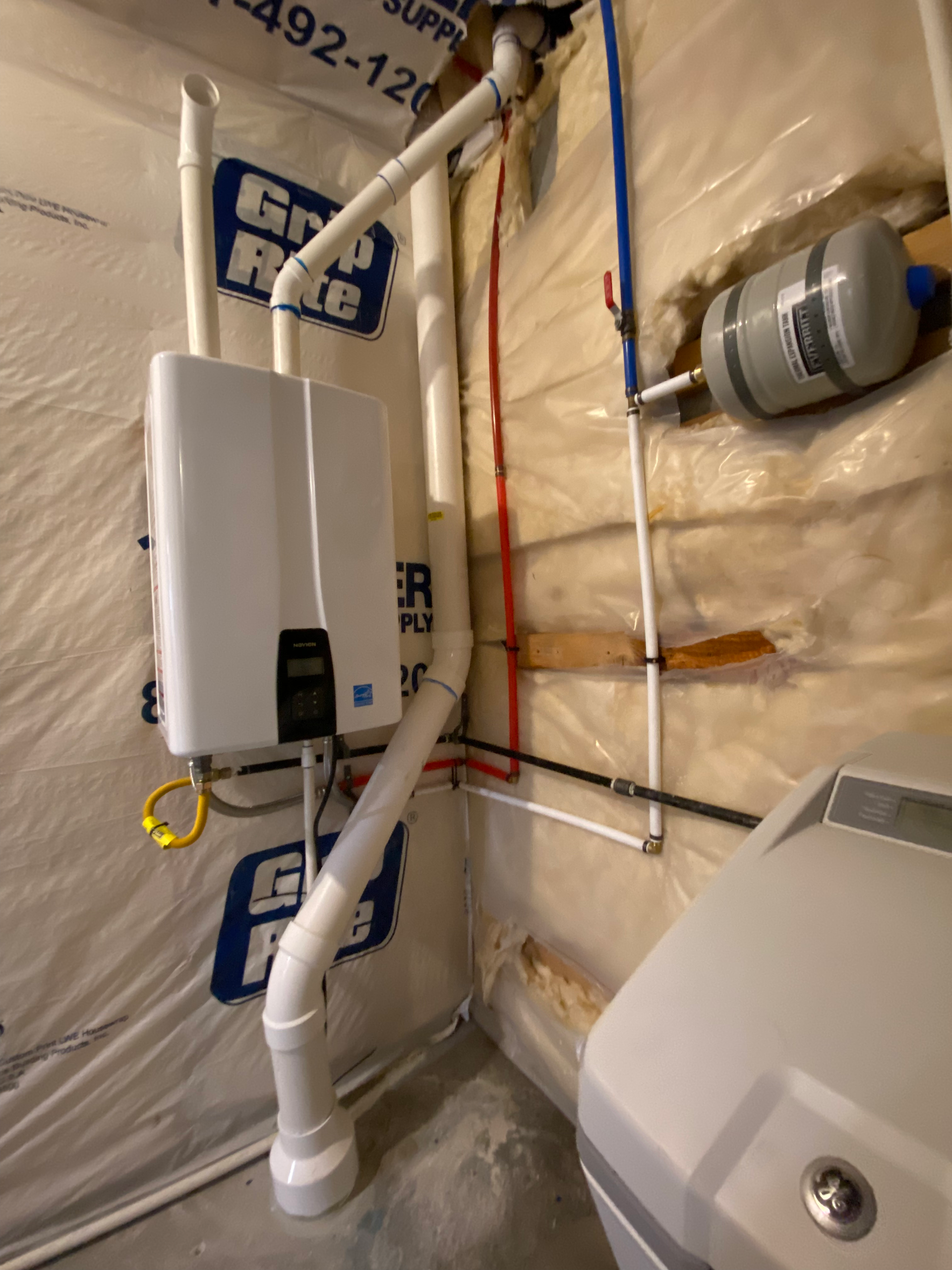 White tankless water heater with pipes in a basement.