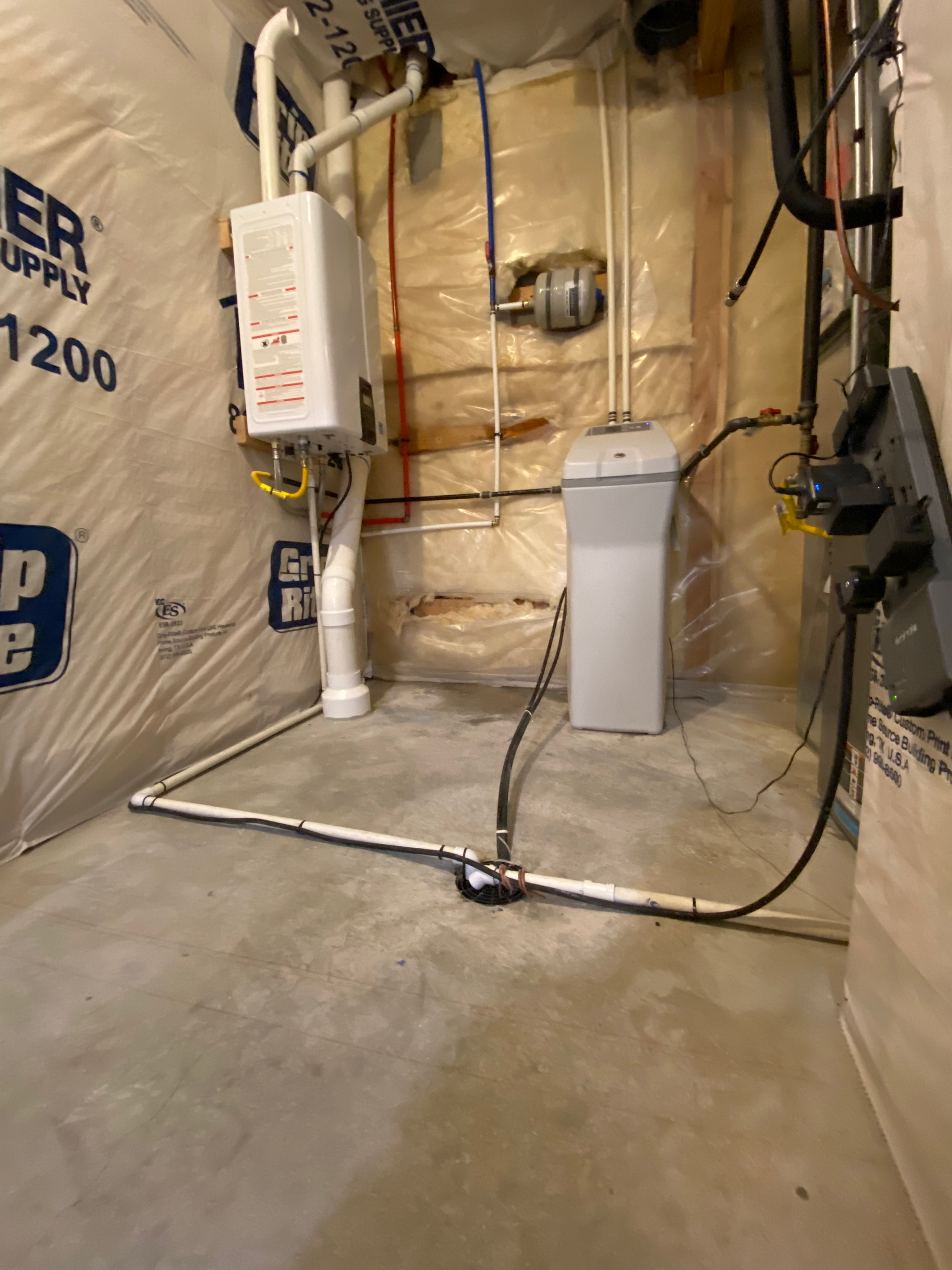 A water heater, water softener, and pipes in a basement utility room.
