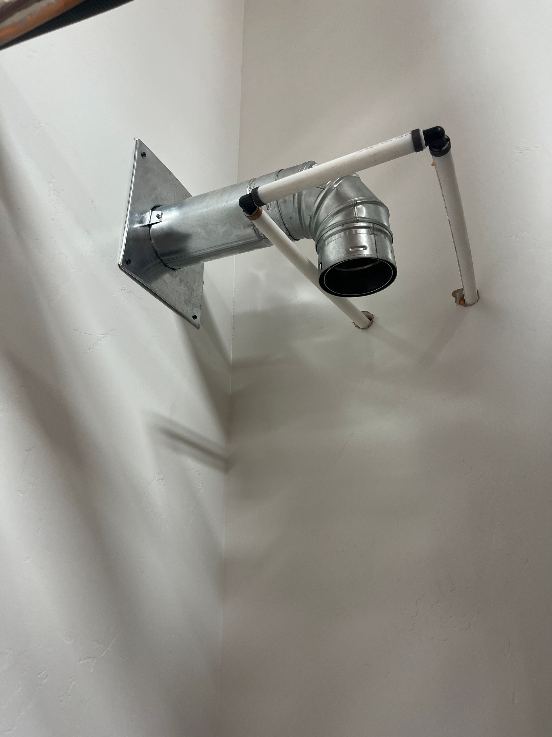 Metal ductwork with attached white pipes, mounted on a white wall.