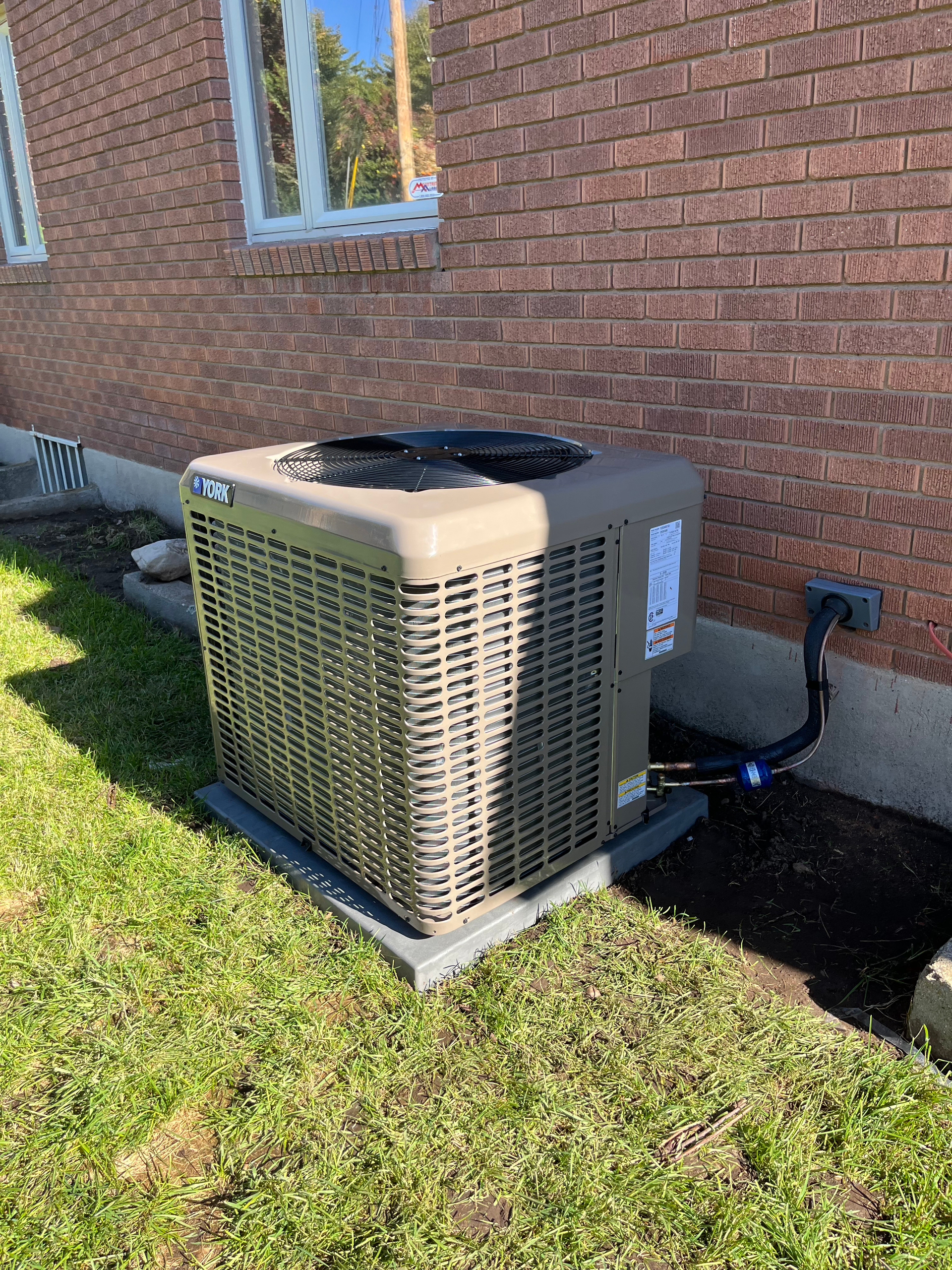 Air conditioning unit outside a brick building on a grassy lawn.