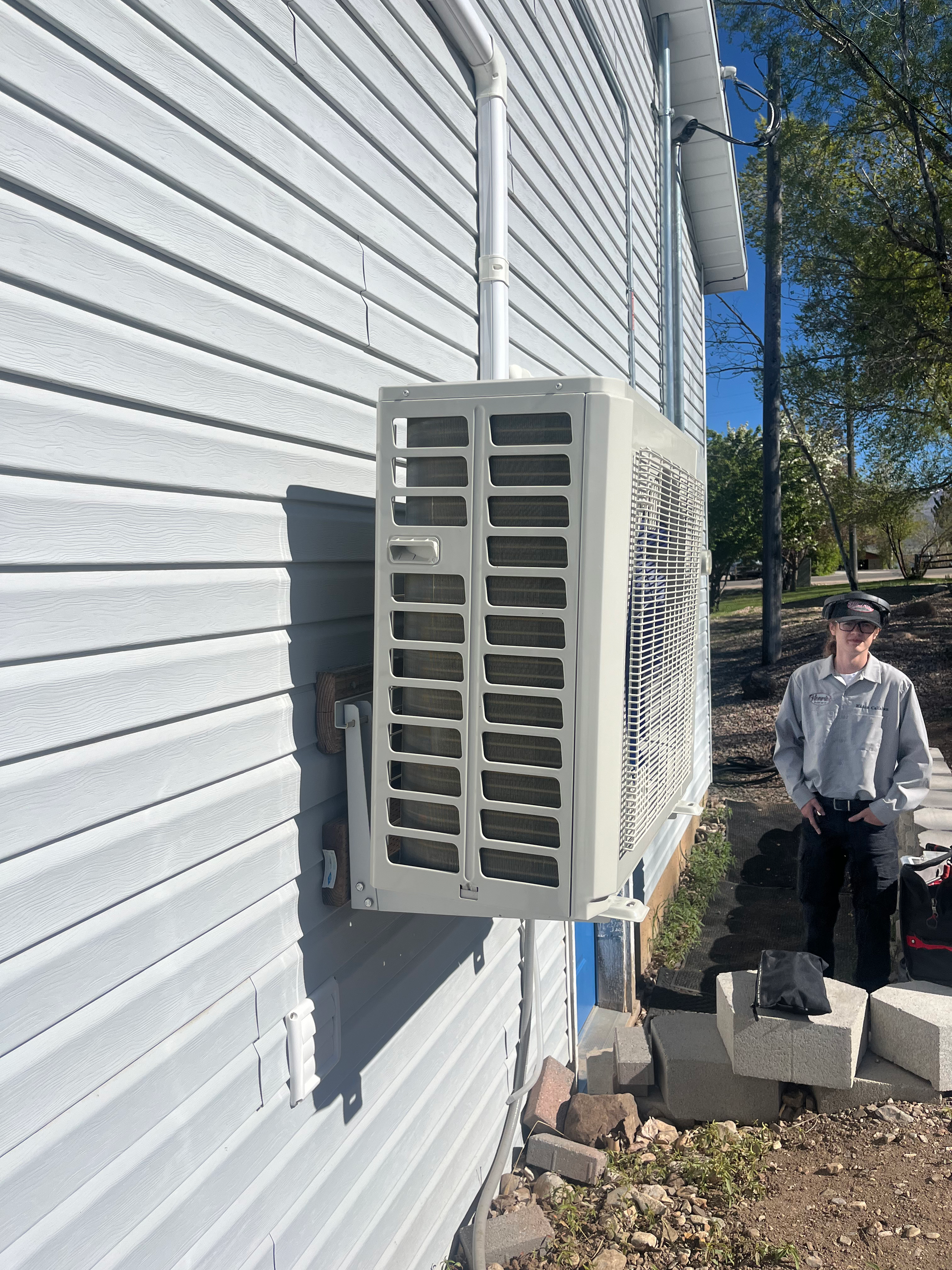 HVAC unit installed on a gray siding building with a man standing nearby.