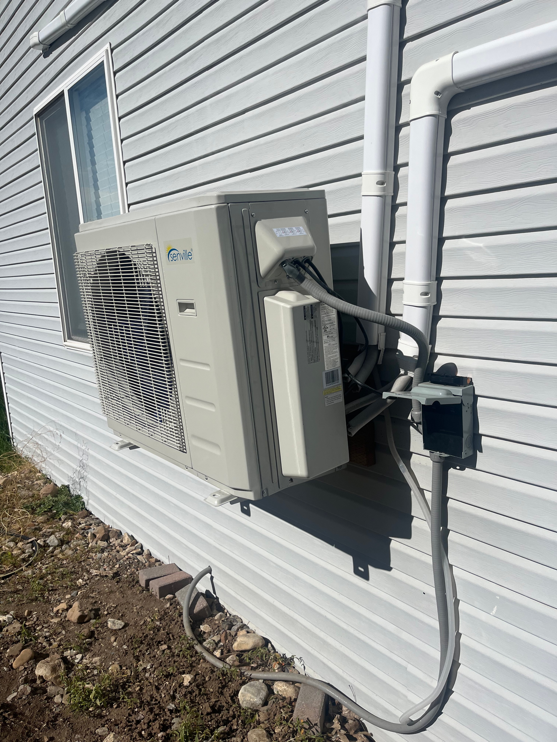 Exterior air conditioning unit mounted on a light gray siding wall with electrical conduit.