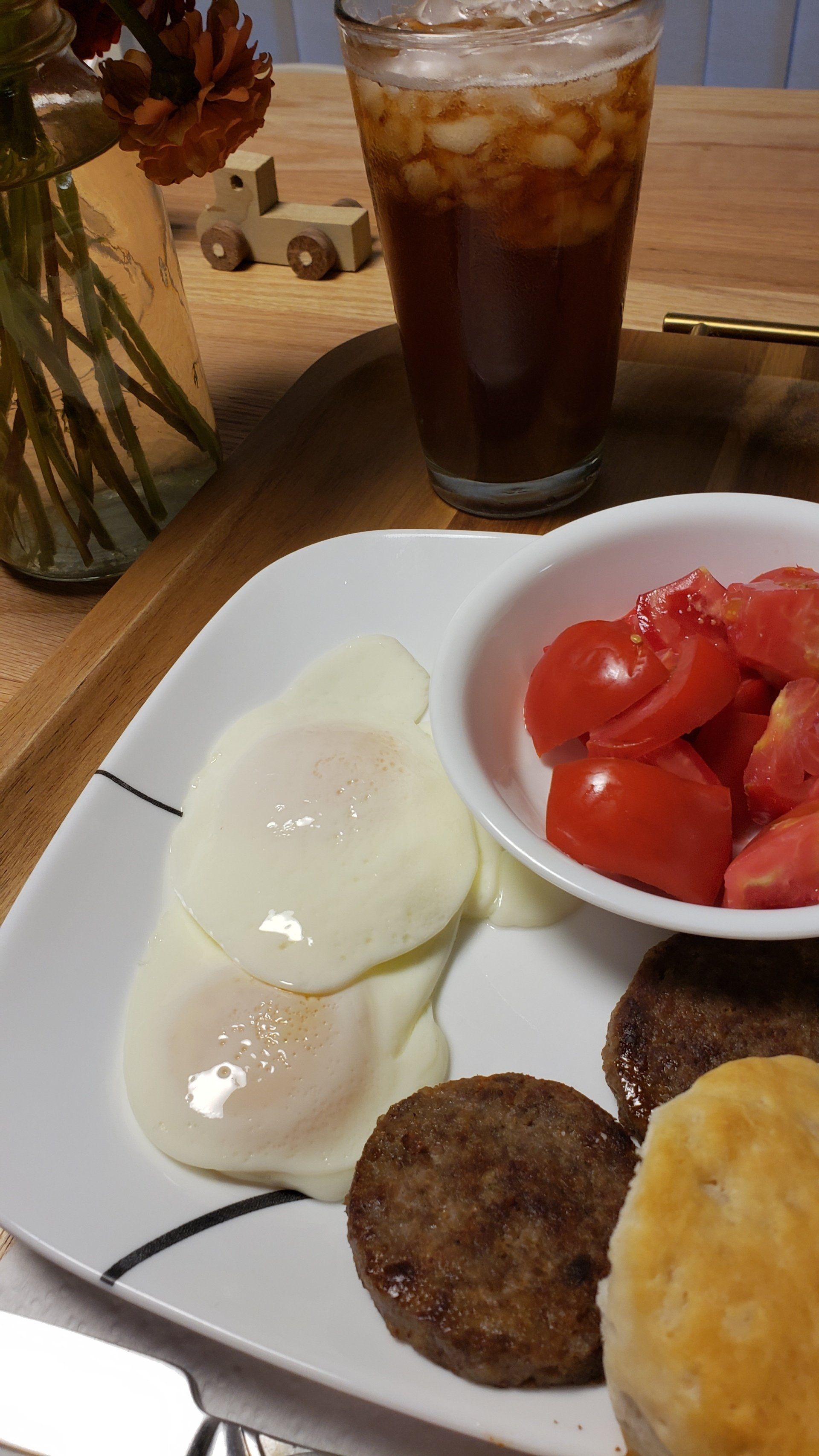 A plate of food with eggs sausage and tomatoes next to a glass of iced tea