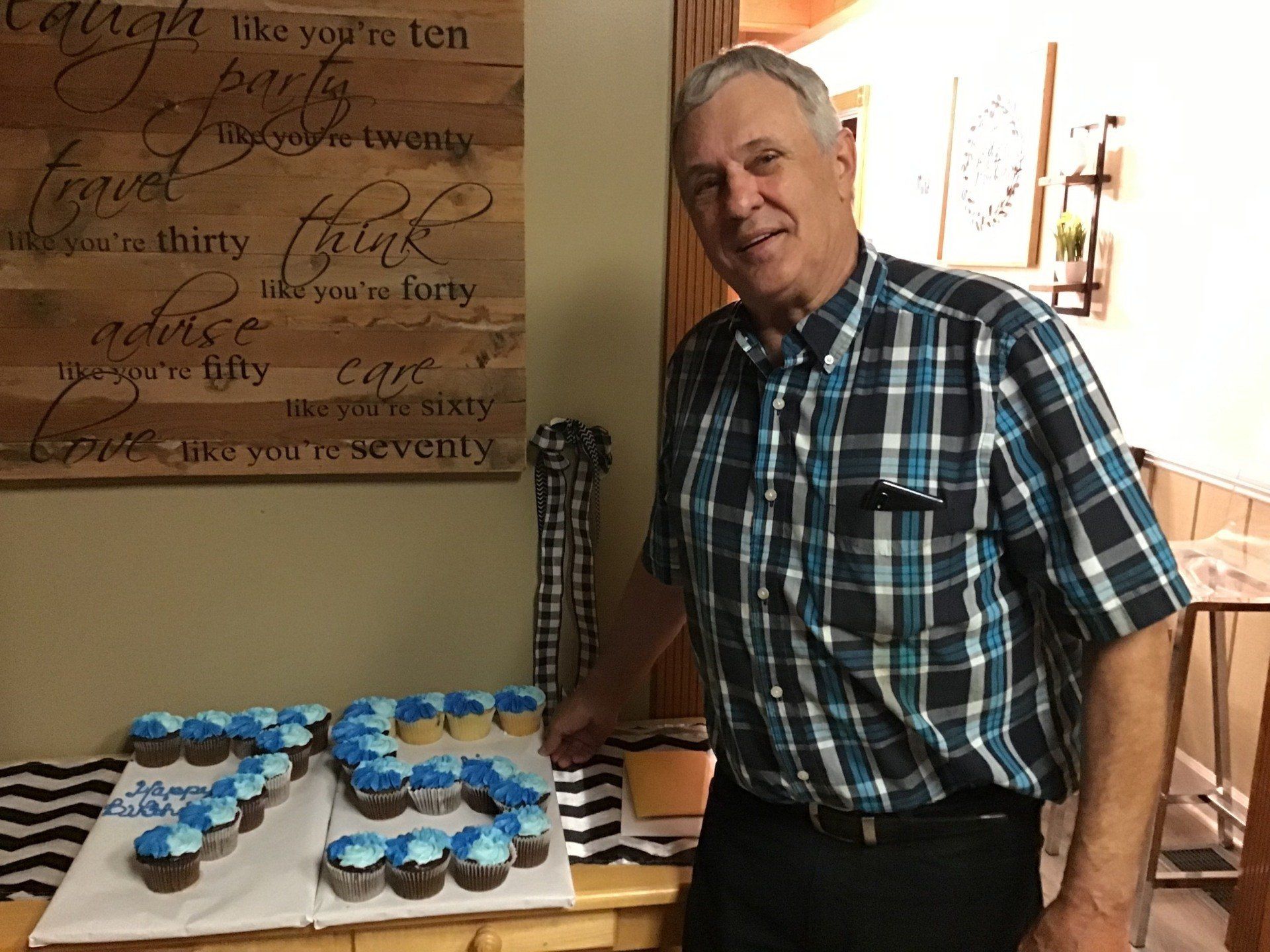 A man in a plaid shirt is standing in front of a table with cupcakes on it.