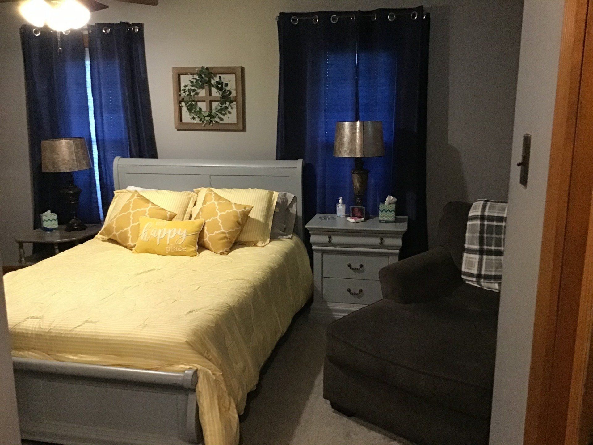 A bedroom with a bed , nightstand , chair and window.