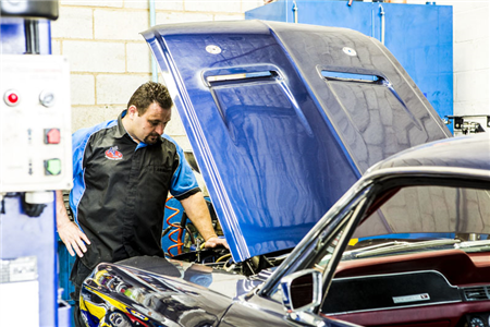 A man is working on a blue car in a garage with the hood open.