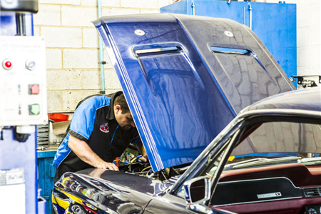 A man is working on a blue car with the hood up in a garage.