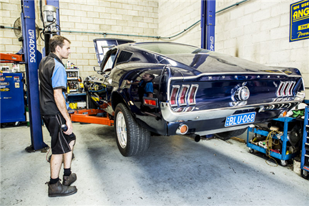A man is standing next to a mustang on a lift in a garage.