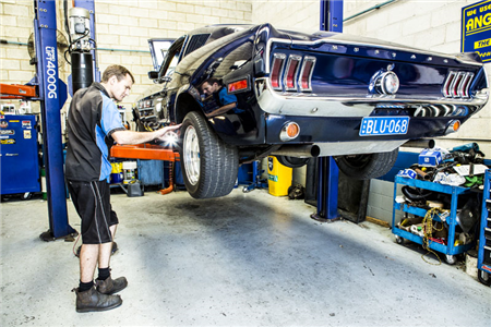 A man is working on a mustang on a lift in a garage.