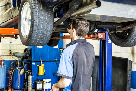 A man is working under a car on a lift in a garage.