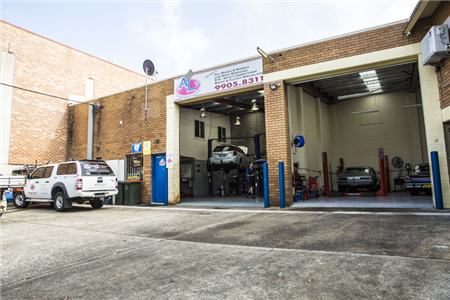 A white truck is parked in front of a car repair shop.