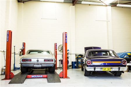 Two cars are sitting on a lift in a garage.