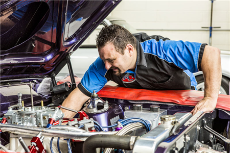 A mechanic is working on the engine of a purple car.
