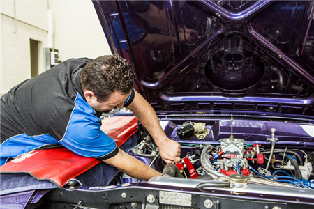 A man is working on the engine of a purple car.