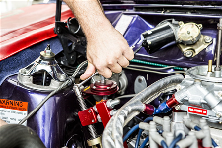 A person is working on a car engine with a warning sign on the hood.