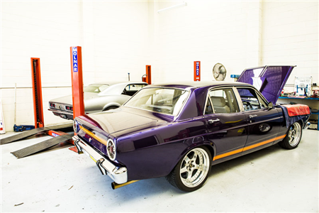 A purple car is parked in a garage with its hood up.