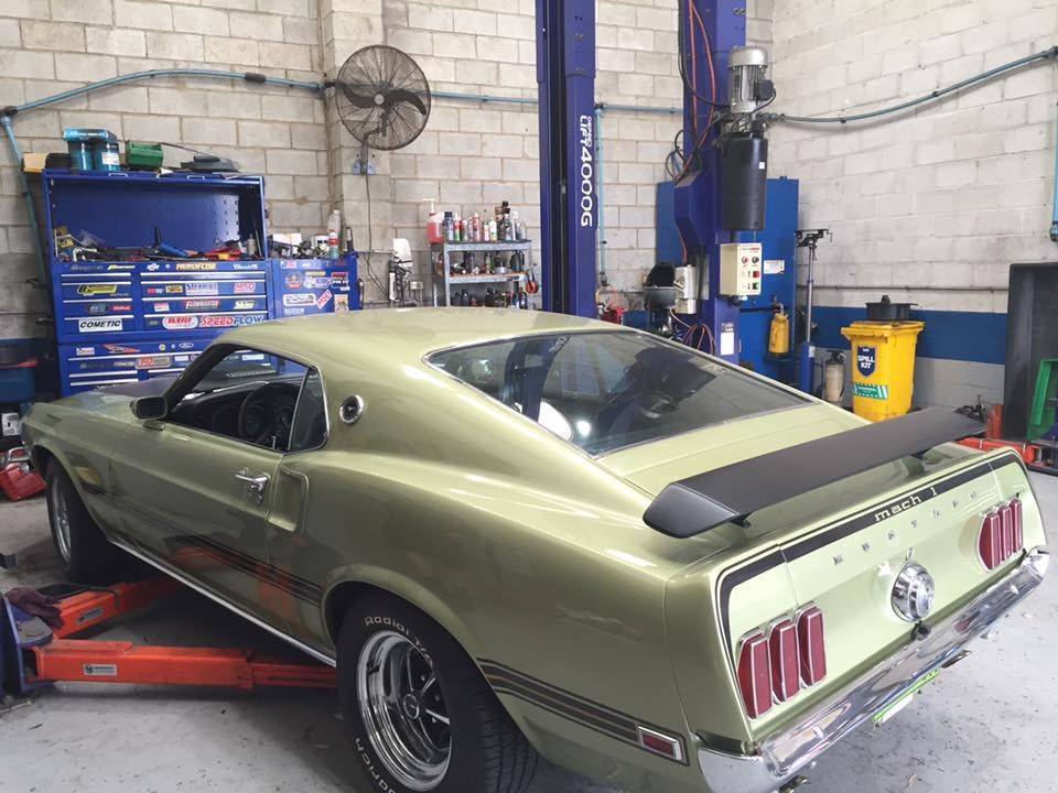 A green mustang is parked on a lift in a garage.
