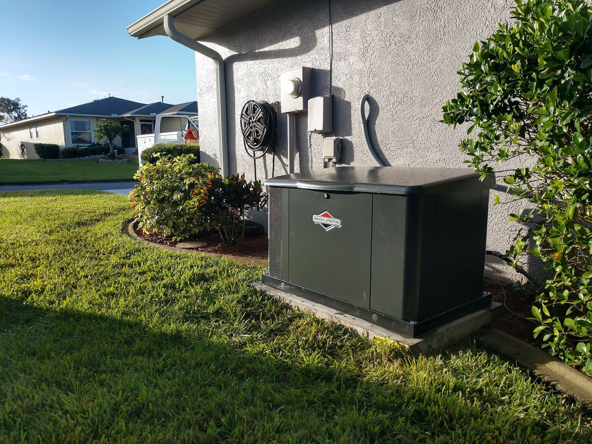Green outdoor generator next to a house with beige stucco siding and landscaping.