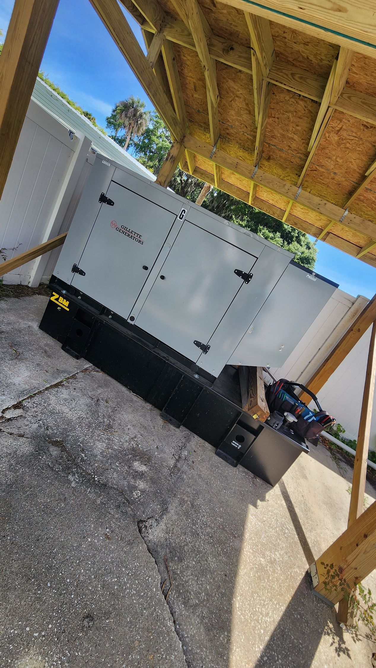 Gray generator with open doors, under a wooden structure, outdoors.