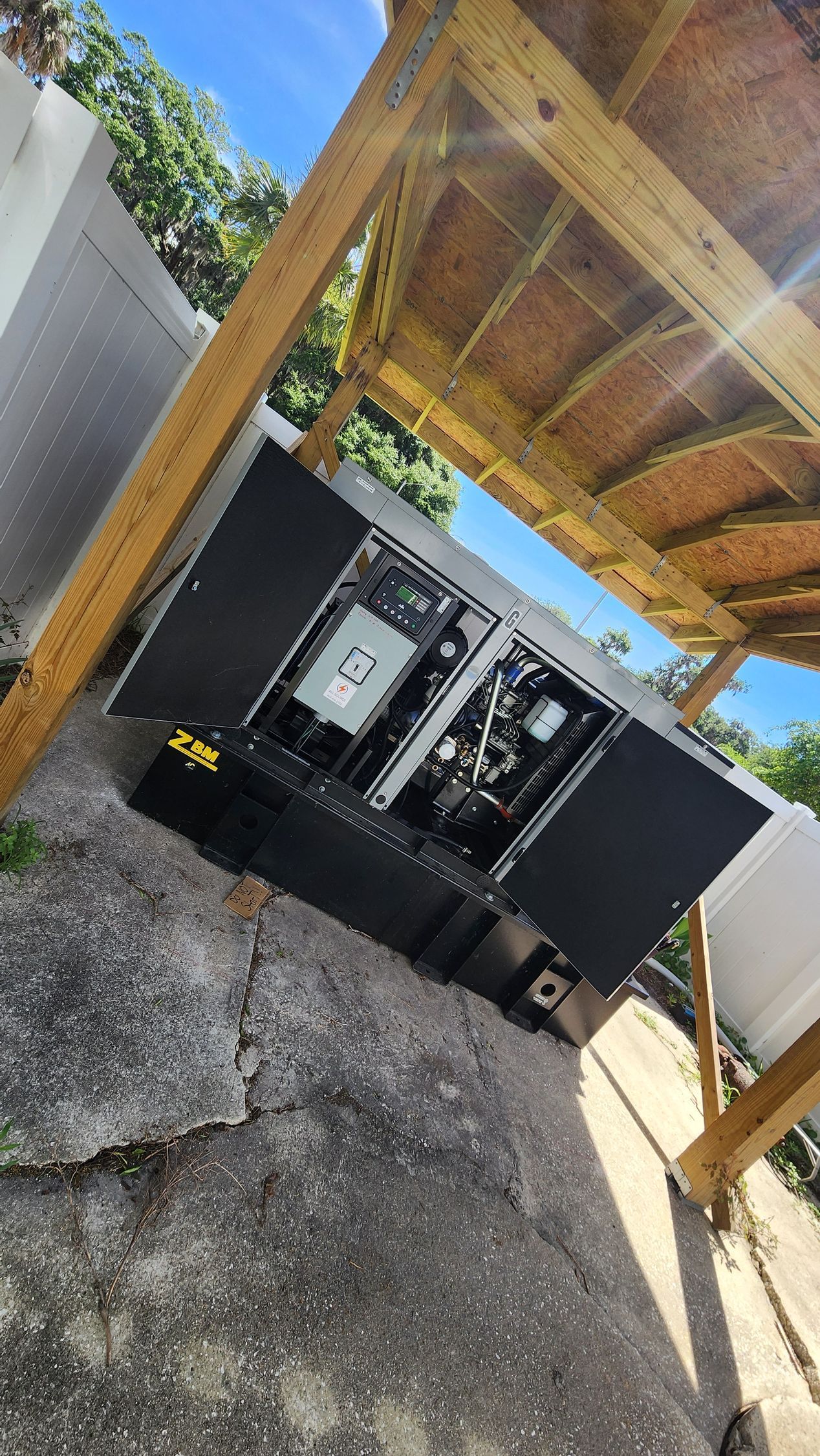 Generac generator outside on gravel next to a bush and wall. Orange stop tag on front.