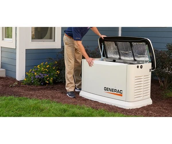 Person in yellow hard hat and work uniform inspecting control panel, holding clipboard.